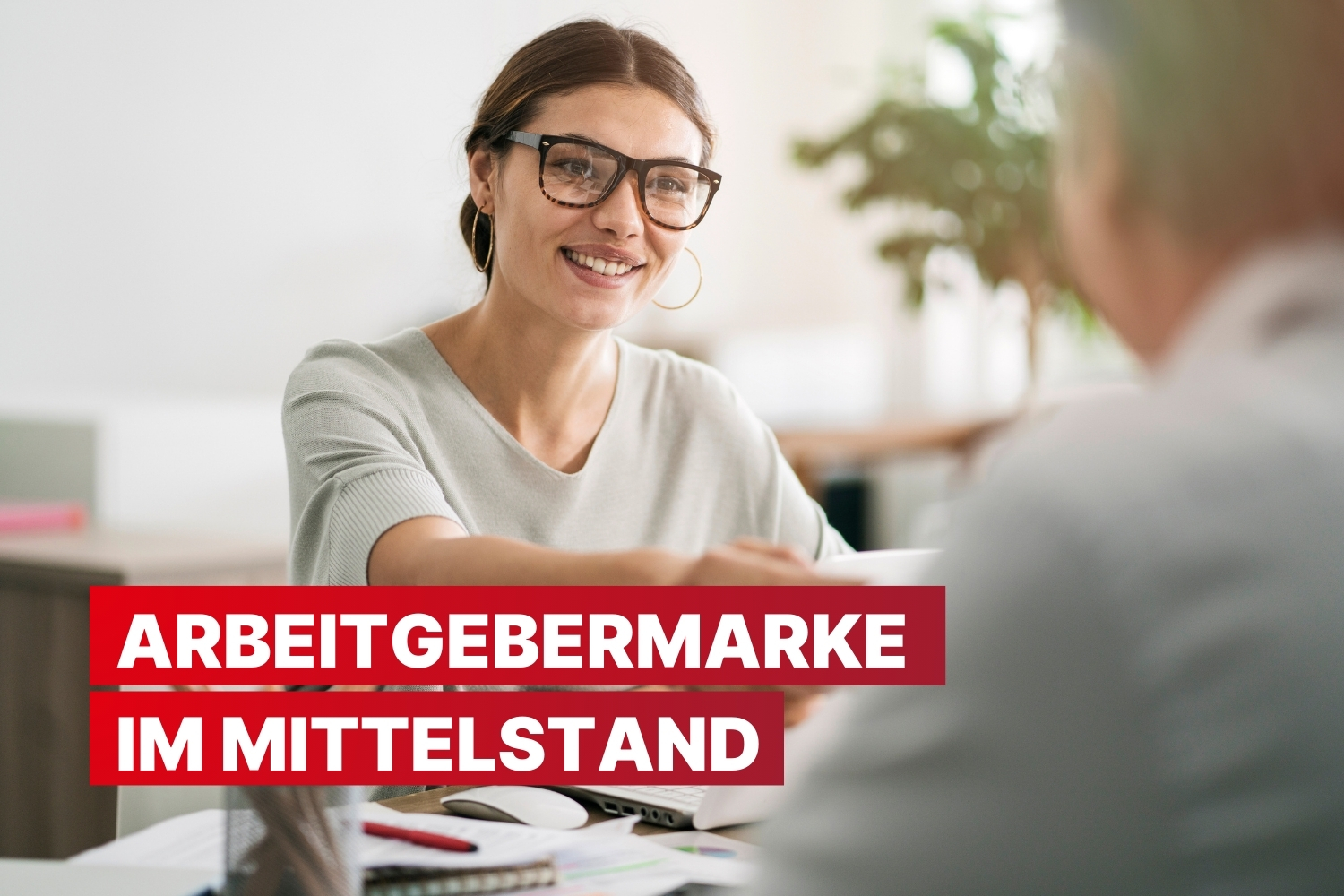 Eine lächelnde Frau mit Brille im Gespräch; rote Schrift im Vordergrund: „Arbeitgebermarke im Mittelstand.“ Büroumgebung im Hintergrund.