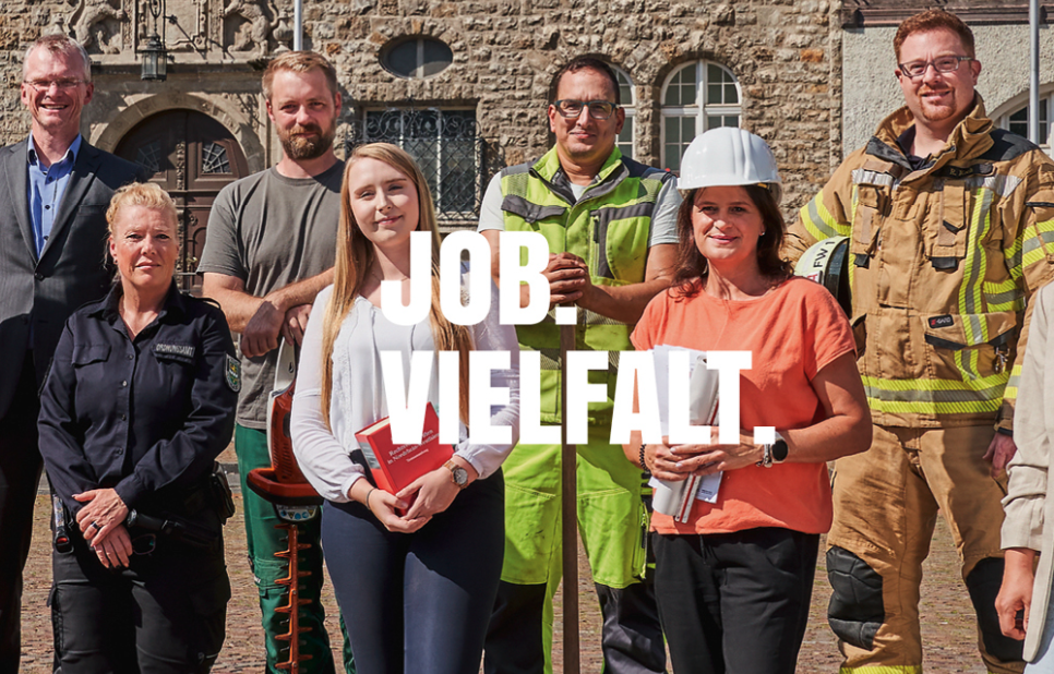 Eine vielfältige Gruppe von Mitarbeitenden in unterschiedlicher Berufsbekleidung steht zusammen. Im Vordergrund steht der Slogan "JOB. VIELFALT.".
