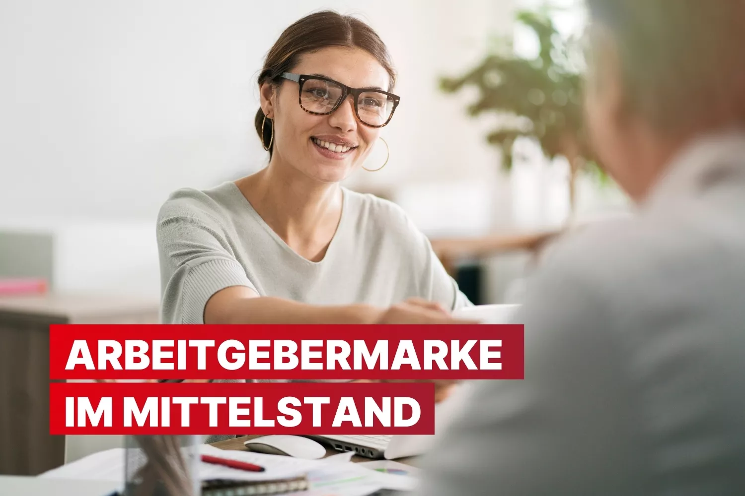 Eine lächelnde Frau mit Brille im Gespräch; rote Schrift im Vordergrund: „Arbeitgebermarke im Mittelstand.“ Büroumgebung im Hintergrund.